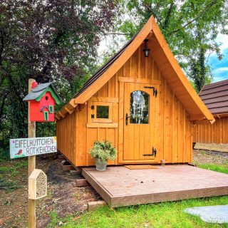 Holzhütte des Models TROLL auf einer Wiese. Vor dem Haus steht ein Pfosten mit einem Vogelhaus.